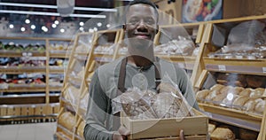 Slow motion portrait of African American salesman holding fresh bread smiling looking at camera in supermarket