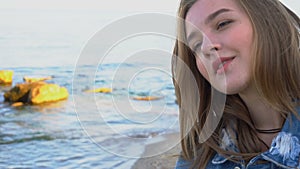 Slow motion portrait of beautiful girl with light smile on lips that poses on camera, standing against blue sea and