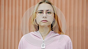 Slow motion portrait of beautiful young woman blonde wearing glasses standing outdoors with serious face