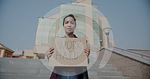 Slow motion portrait of biracial woman holding Work Hard sign motivating and inspiring effort standing in city
