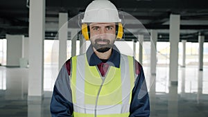 Slow motion portrait of builder wearing safety clothing and headphones standing in commercial building