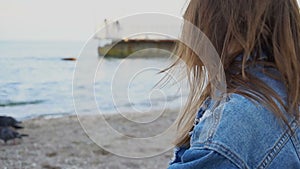 Slow motion portrait of cheerful girl who posing at camera and cute laughing while sitting on beach against blue sea and