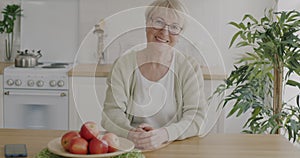 Slow motion portrait of cheerful senior woman sitting in kitchen at table smiling looking at camera