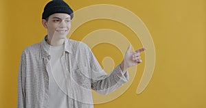 Slow motion portrait of cheerful teenager pointing sidewards and smiling on yellow background