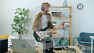 Slow motion portrait of cheerful young man playing electric guitar and singing having fun at home