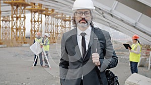 Slow motion portrait of construction project manager standing outdoors wearing helmet and suit