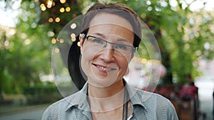 Slow motion portrait of elegant woman in glasses smiling outdoors in summer