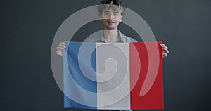 Slow motion portrait of French student holding national flag of France smiling on grey color background