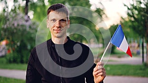 Slow motion portrait of Frenchman waving national flag looking at camera and smiling with beautiful modern park in