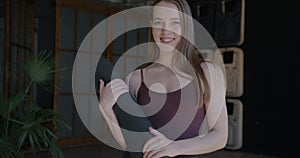 Slow motion portrait of good-looking young woman with yoga mat standing in cozy studio smiling