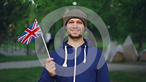 Slow motion portrait of handsome Englishman in sports clothes holding official British flag looking at camera and