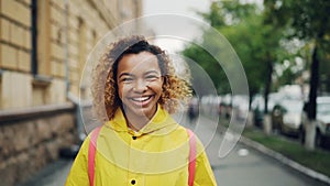 Slow motion portrait of happy African American girl smiling and looking at camera standing outdoors with green trees and