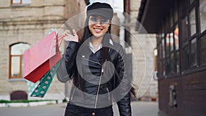 Slow motion portrait of happy Asian girl holding shopping bags, walking home from store then turning and looking at