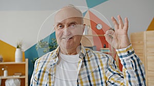 Slow motion portrait of happy senior man showing OK hand gesture at home