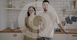 Slow motion portrait of happy young couple standing in kitchen at home smiling looking at camera