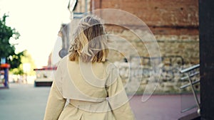 Slow motion portrait of happy young lady in elegant garment walking in the street, smiling and looking at camera