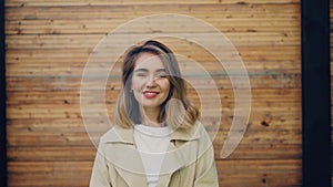 Slow motion portrait of happy young woman with blond hair looking at camera and smiling then laughing standing outdoors