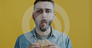 Slow motion portrait of hungry young man eating burger biting chewing enjoying taste on yellow background