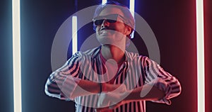 Slow motion portrait of joyful man with illuminated glasses dancing in night club with neon lamps
