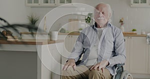 Slow motion portrait of quiet senior man sitting in modern wheelchair in kitchen at home