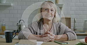 Slow motion portrait of senior woman smiling sitting at kitchen table at home