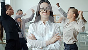 Slow motion portrait of serious Asian woman standing among dancing smiling people in office