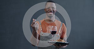 Slow motion portrait of smiling African American waiter holding food order making hand gesture asking to pay on grey
