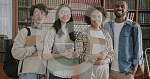 Slow motion portrait of students diverse group standing in university library holding books smiling looking at camera