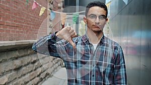 Slow motion portrait of unhappy Middle Eastern man showing thumbs-down hand gesture outdoors