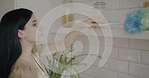 Slow motion portrait of young lady dusting shelf in kitchen concentrated on housework