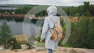 Slow motion portrait of young woman tourist with backpack walking to the edge of cliff with beautiful view of lake and