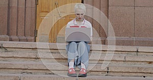 Slow motion portrait of young woman working with laptop computer typing sitting on stairs on campus outdoors