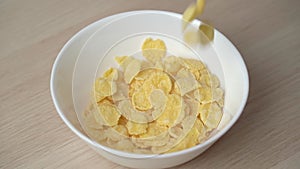 Slow motion of pouring corn flakes in a white plate close up.