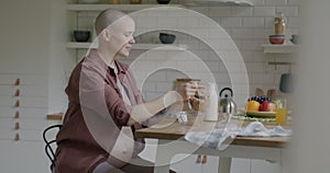 Slow motion of pregnant young woman eating healthy breakfast sitting at table in kitchen at home