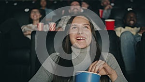 Slow motion of pretty brunette enjoying film in cinema laughing eating popcorn