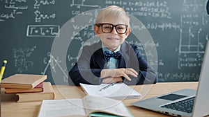 Slow motion of prodigy kid in university classroom at desk with chalkboard in background
