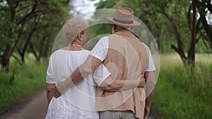 Slow motion. Rear view. Older married couple hugging while standing in a city park on a summer day outdoors. An elderly