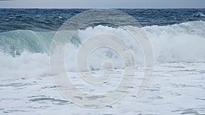 Slow motion sea surf during a storm. Huge storm waves roll onto the shore covered with white foam. Boundless and