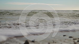 Slow motion of sea waves washing northern sandy beach with water and foam. Camera moves along stormy ocean coastline in