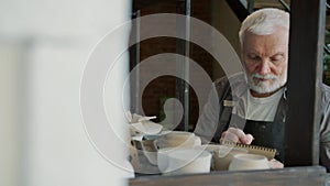 Slow motion of senior ceramist counting pots and vases in workshop writing info