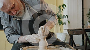Slow motion of senior man potter making vase on spinning wheel working alone