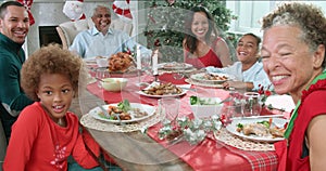 Slow motion sequence of family with grandparents sitting around table and enjoying Christmas meal - looking at camera