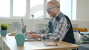 Slow motion of serious retired man working with laptop in house busy with freelance work