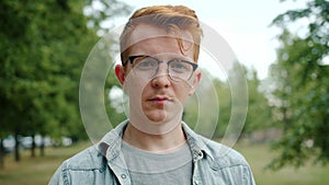 Slow motion of serious young man in glasses standing alone in green park in city