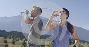 Slow motion shot of a Couple of joggers drinking water, resting after intense training in nature.