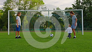 Slow motion shot of family playing soccer in park together. Happy parents and kids playing with ball in green meadow