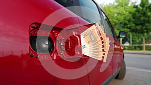 Slow motion shot of fifty euro banknotes attached to an open fuel tank of a car