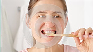 Slow motion shot of young woman brushing her teeth and looking in mirror. Concept of teeth health, self checking mouth and oral