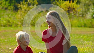 Slow motion shot of a young woman and her little son that sit on a lawn with a bicycle laying next to them