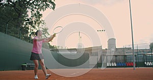 Slow-motion side view of a young athlete trains the serve of the tennis ball. A teenage athlete is playing tennis on a
